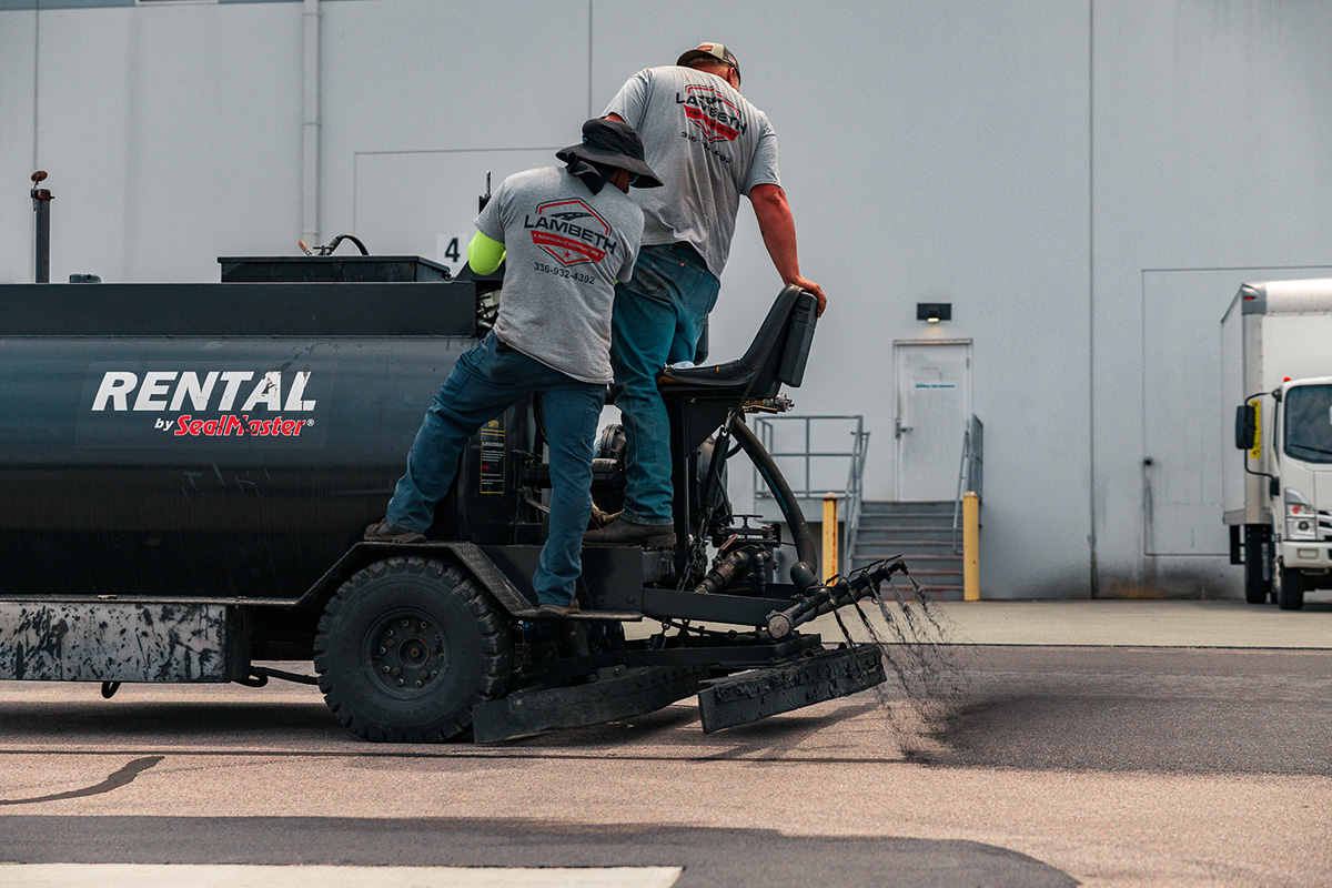 Lambeth Asphalt crew operating a SealMaster ride-on sealcoating machine at the Link Properties warehouse complex in Durham NC