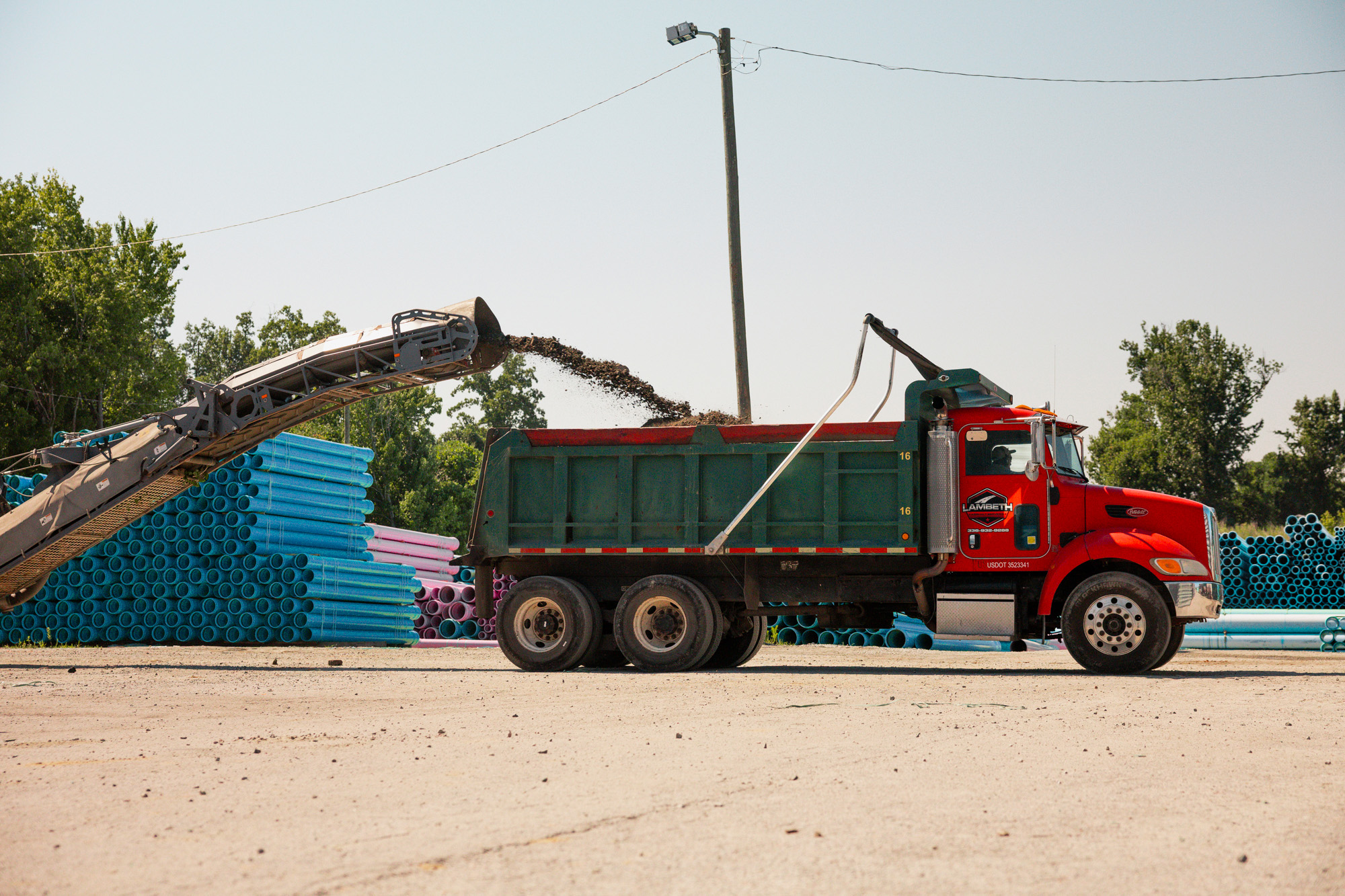 Milling machine conveyor loading reclaimed asphalt into a Lambeth Asphalt Services dump truck at the National Pipeline facility in Colfax, NC.