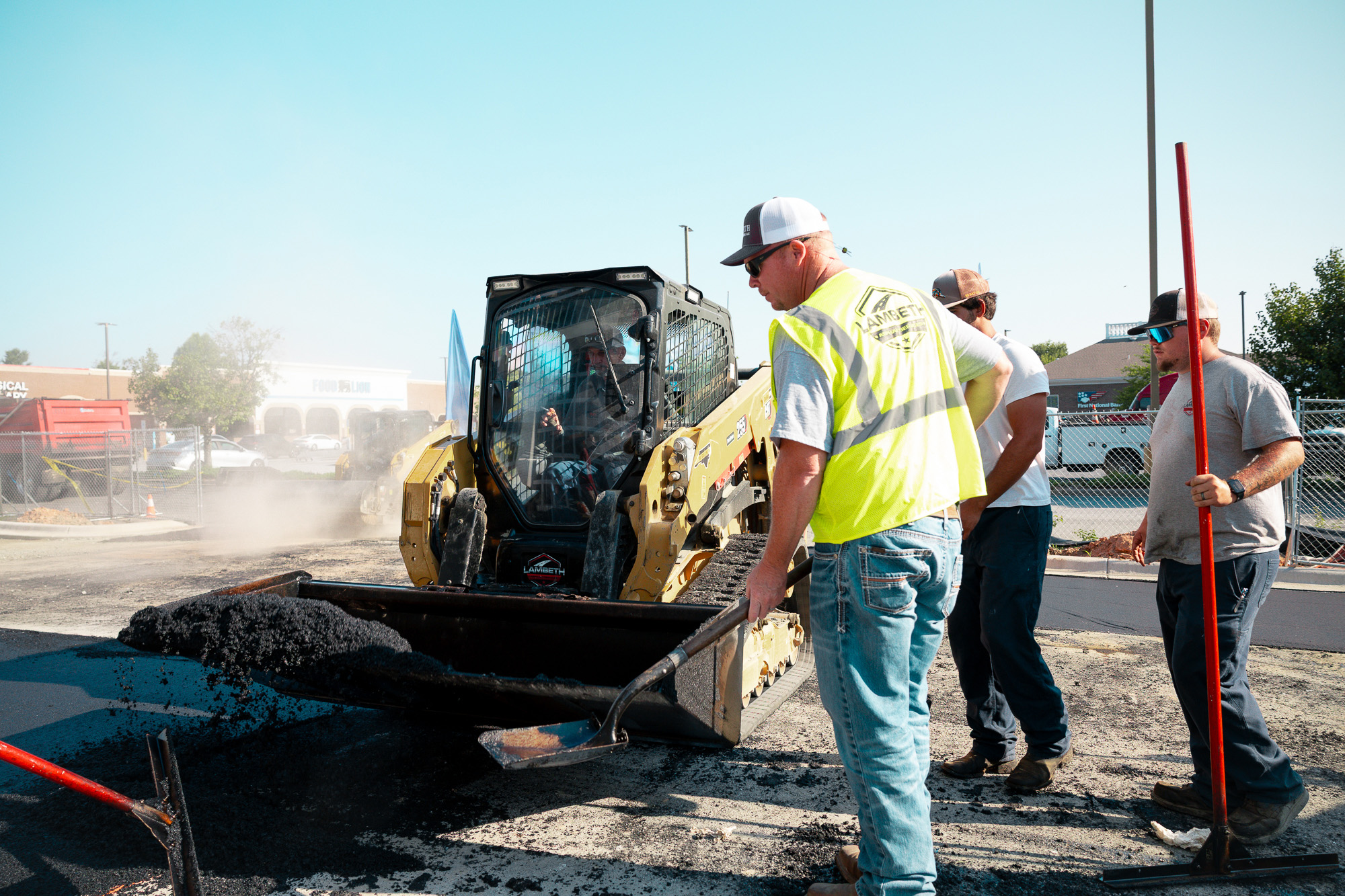 Lambeth Asphalt Services crew guiding a CAT skid steer while loading milled asphalt during parking lot milling and repaving at Mavis Tire in Greensboro, NC.
