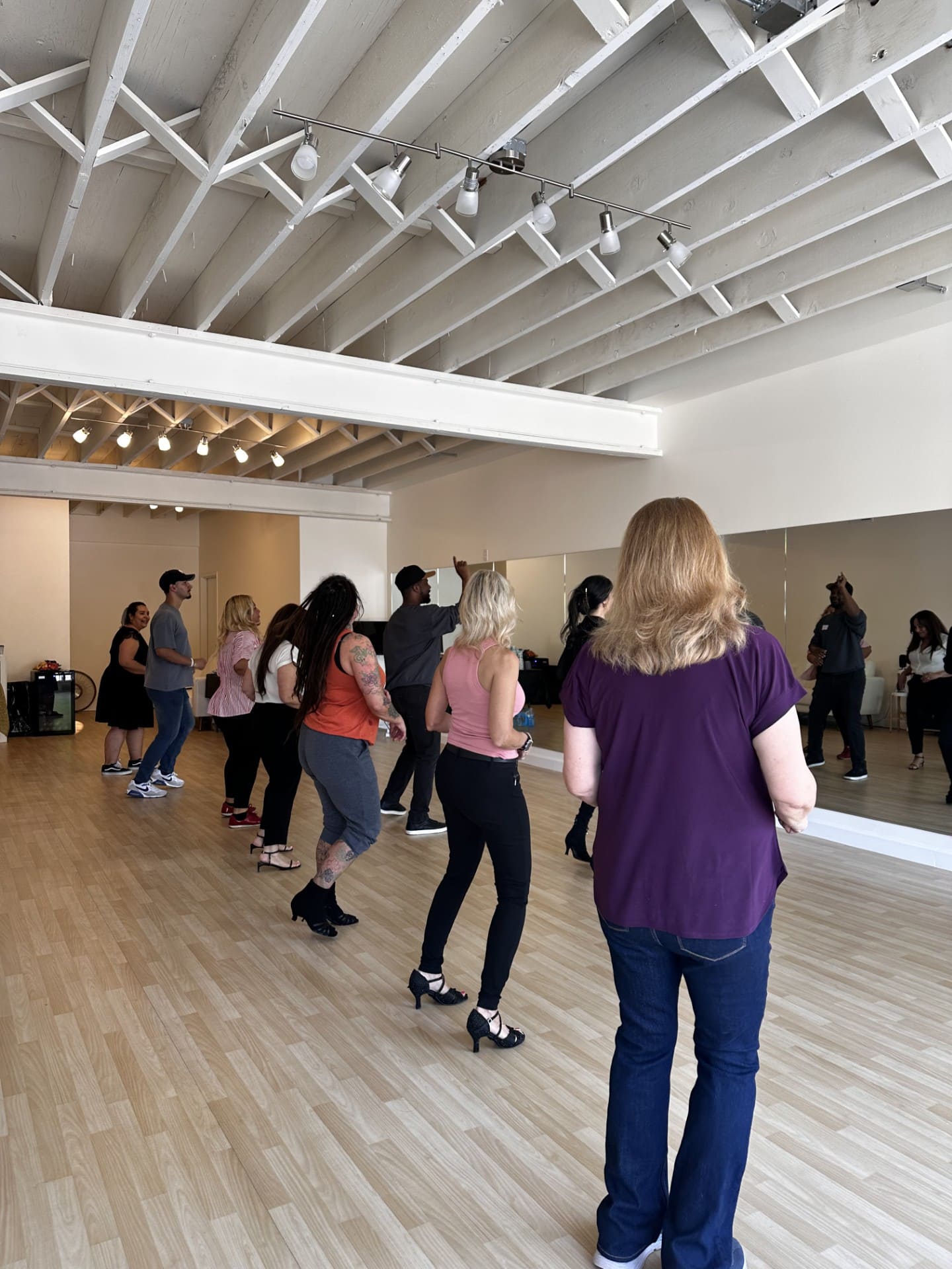Group of people lined up in a studio following a dance instructor by the mirrors.