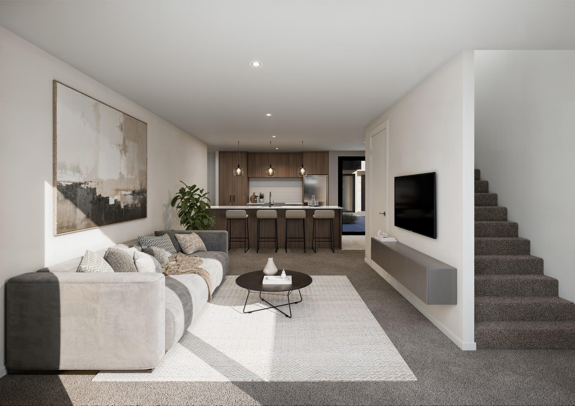 Modern living room with a large beige sectional sofa, a round black coffee table on a white rug, wall-mounted TV, and kitchen with bar stools in the background.