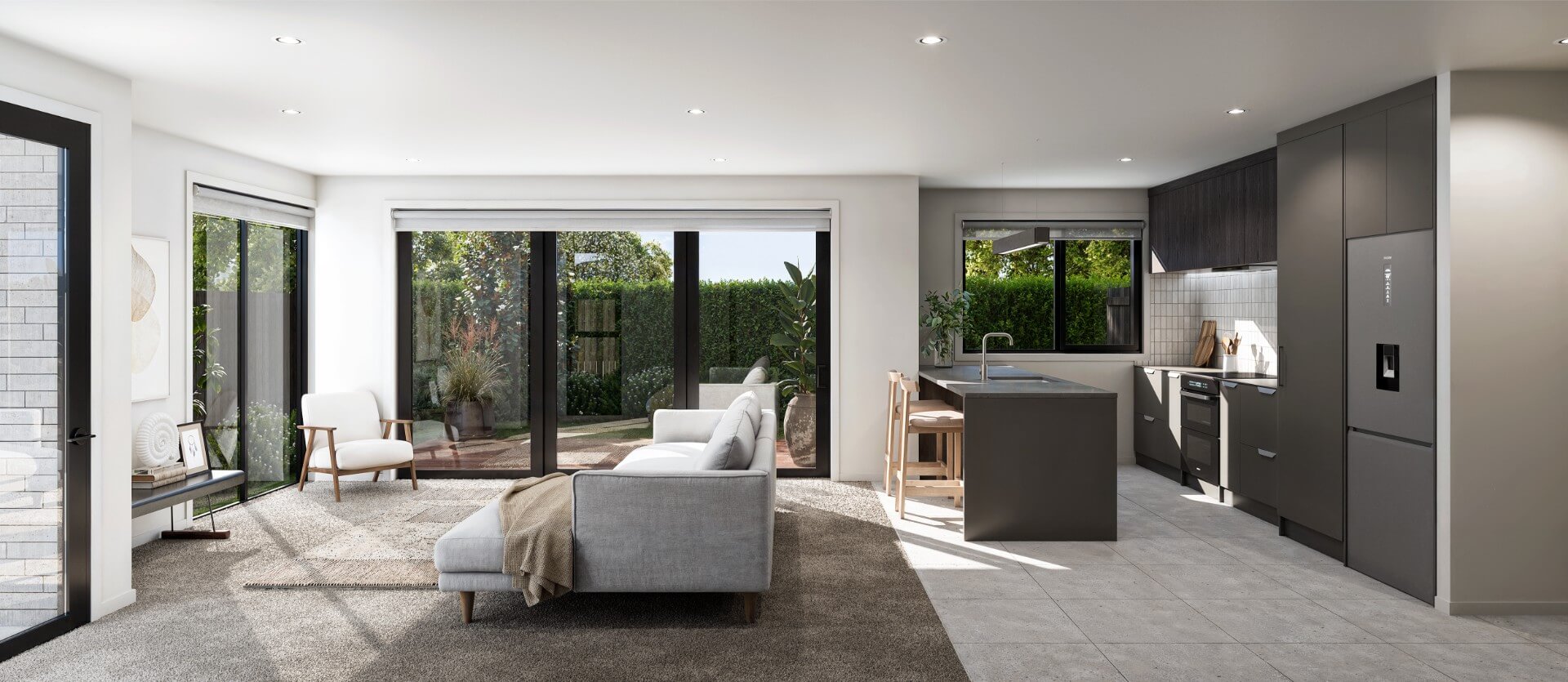 Modern open-plan kitchen and living room with gray sofa, armchair, large windows, and dark kitchen cabinetry with island and bar stools.