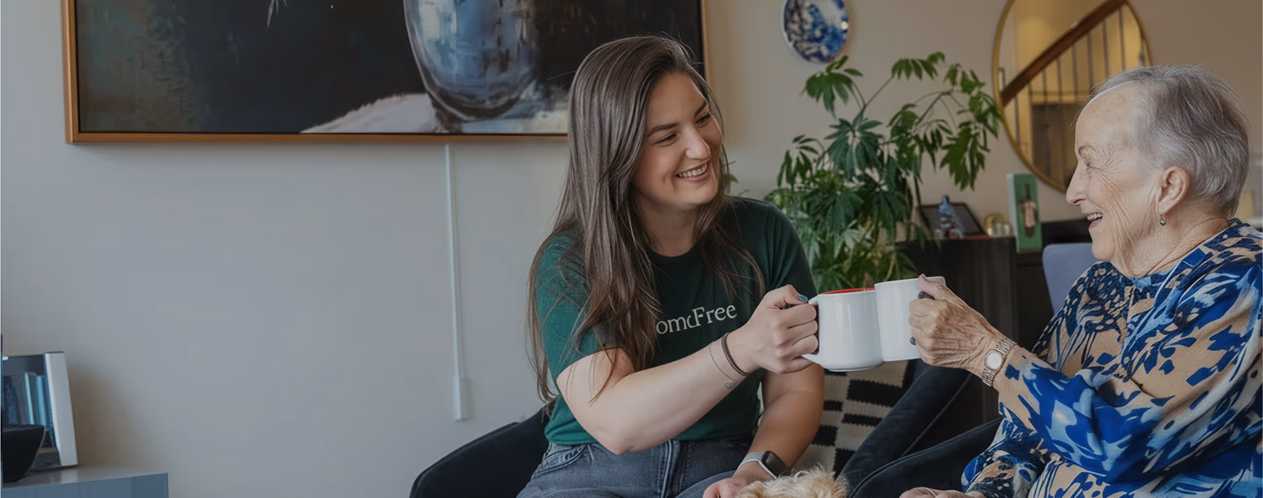 Young woman and elderly woman smiling and clinking white mugs in a cozy living room.