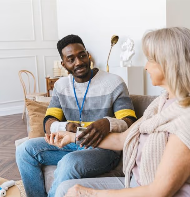 Caregiver checking blood pressure of a seated older woman in a bright living room.