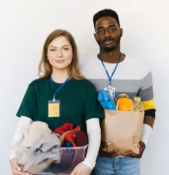Smiling man and woman holding laundry basket and grocery bag standing against white background.