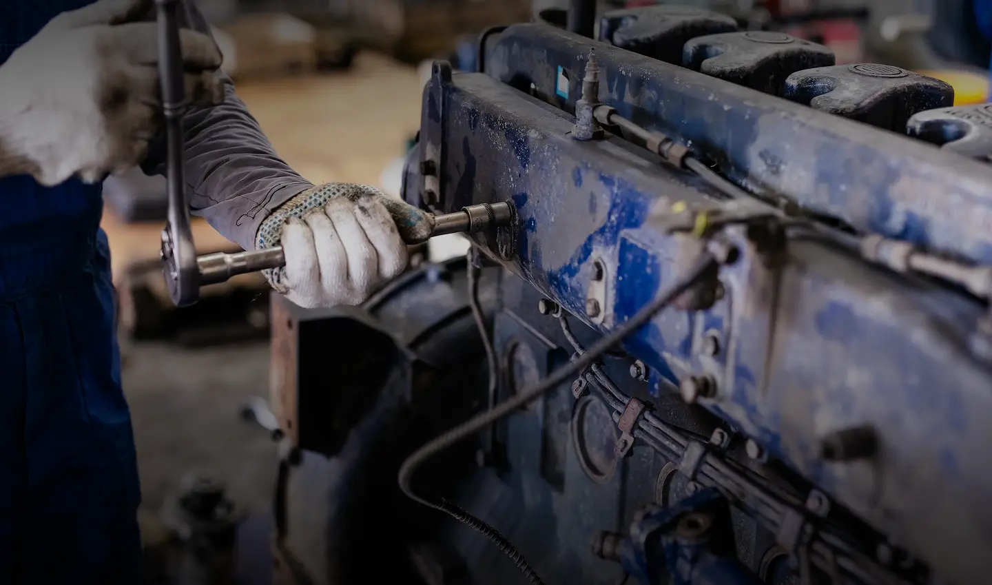 Mechanic wearing gloves using a wrench to repair a large dirty blue engine.
