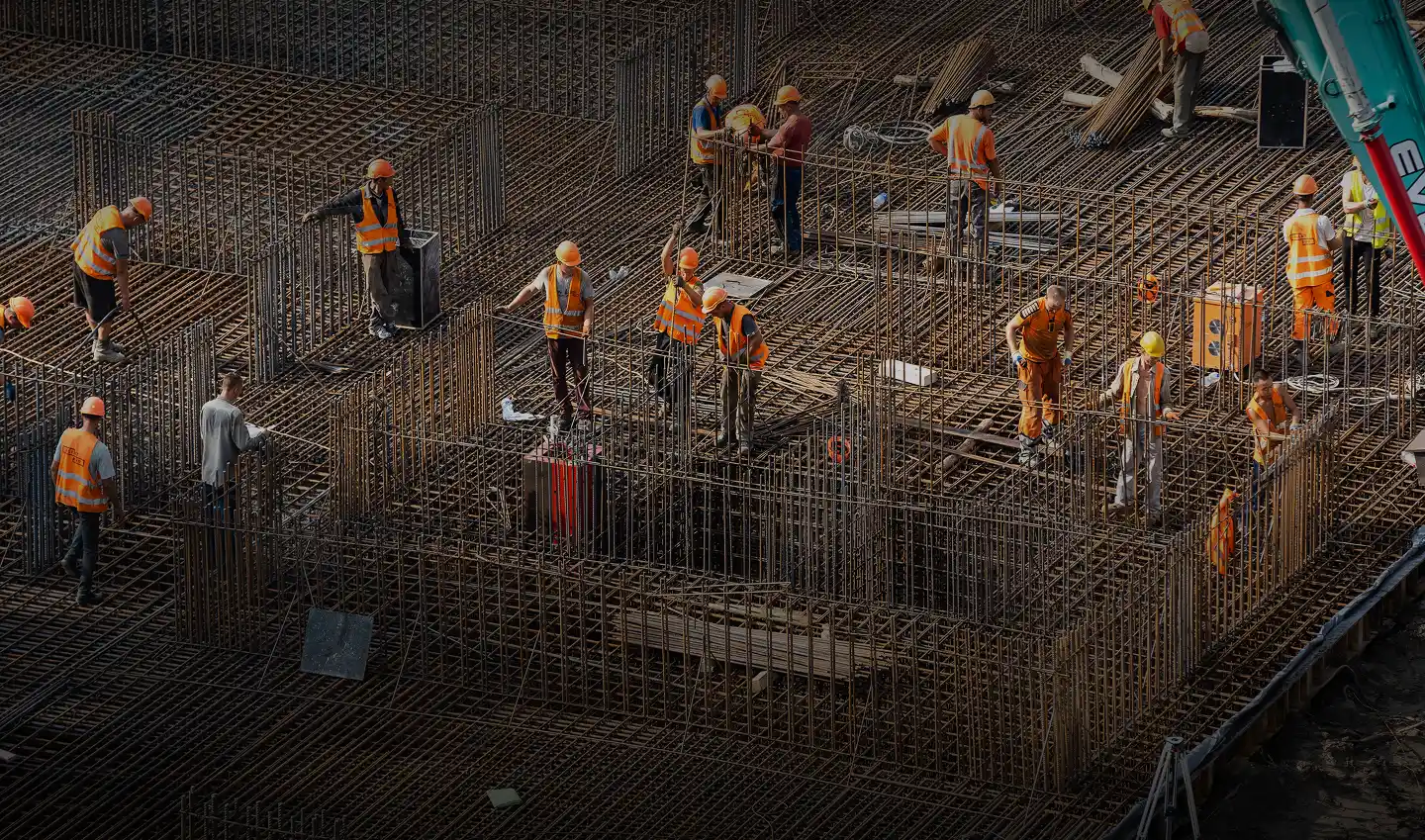 Workers in orange safety vests and helmets assembling steel rebar framework at a construction site.