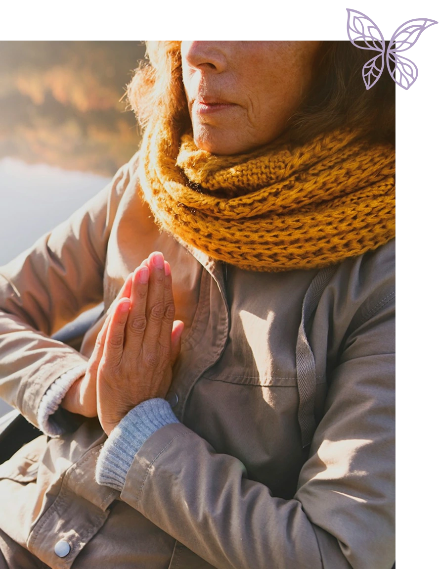 Close-up of a person wearing a mustard yellow knitted scarf and beige jacket with hands pressed together in a prayer or meditation gesture.
