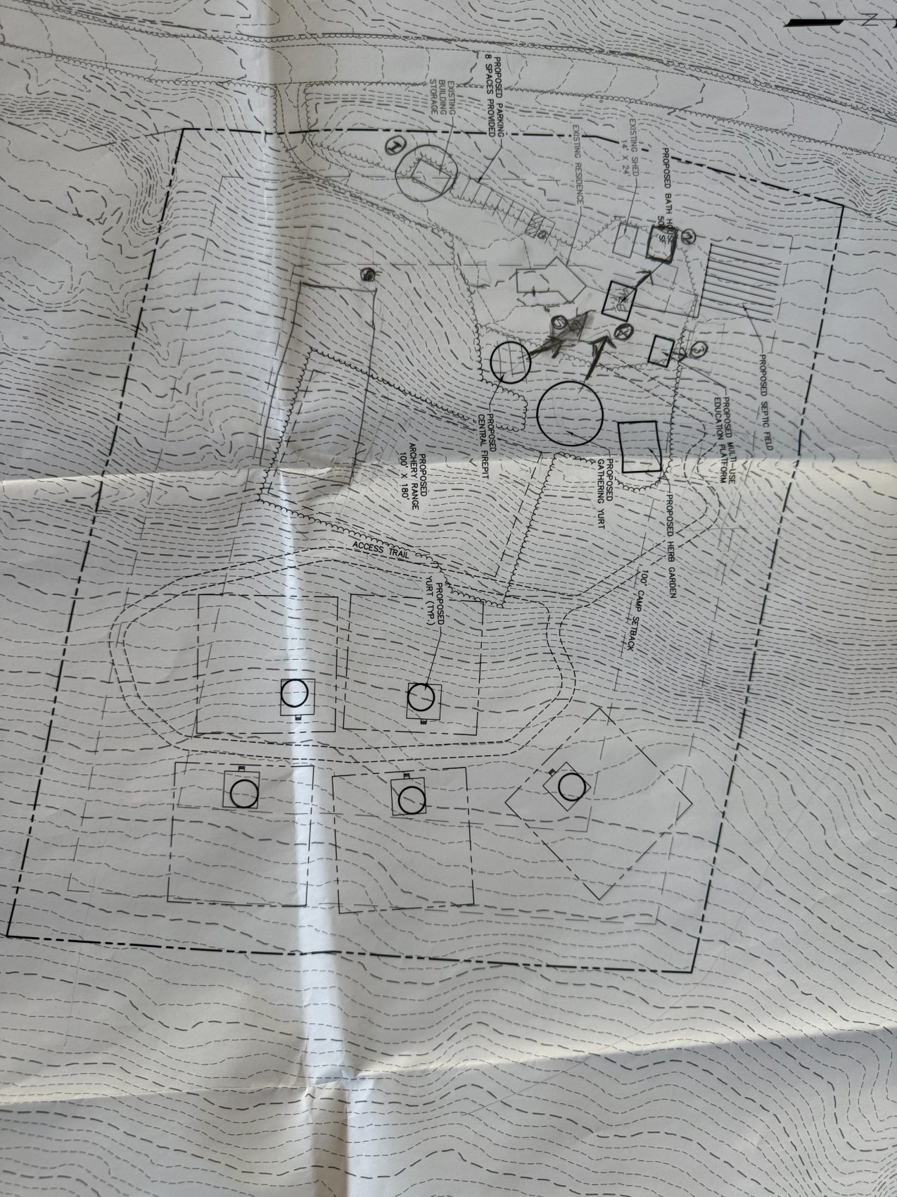 A hand-marked surveyor contour site plan of the property, showing proposed yurts, a central firepit, gathering yurt, archery range, bath house, herb garden and parking.