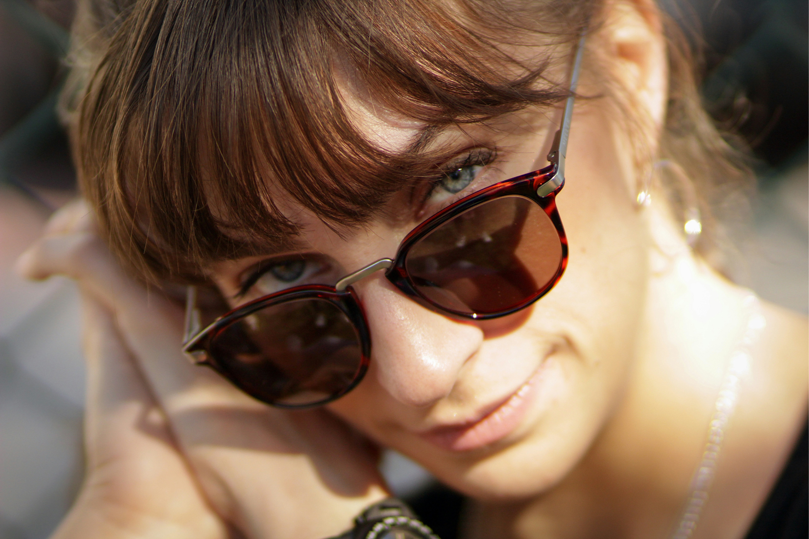 Close-up of a woman wearing tortoiseshell sunglasses, smiling and resting her face on her hand.
