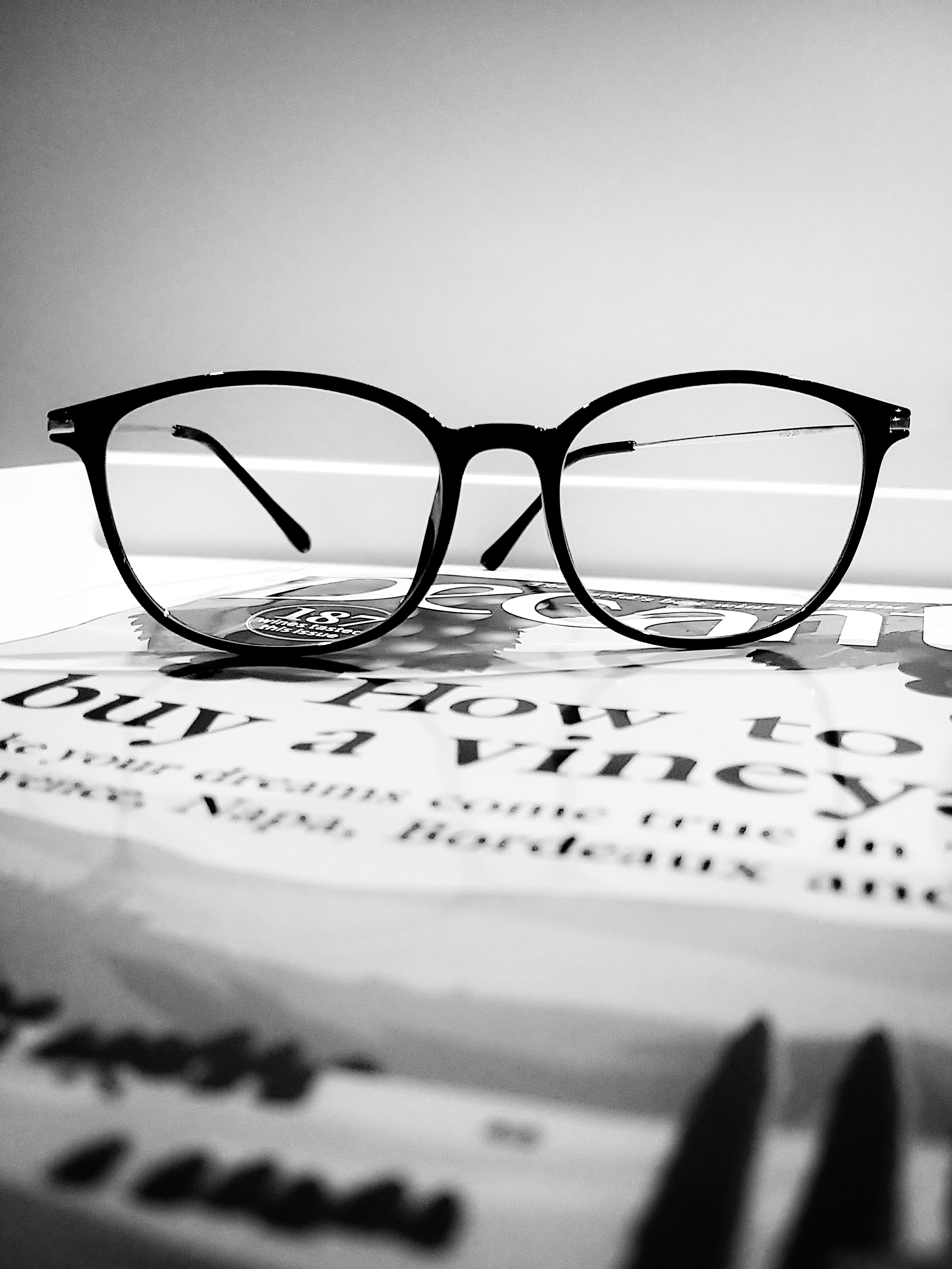 Black-rimmed glasses resting on a magazine titled 'How to buy a vineyard' in black and white.