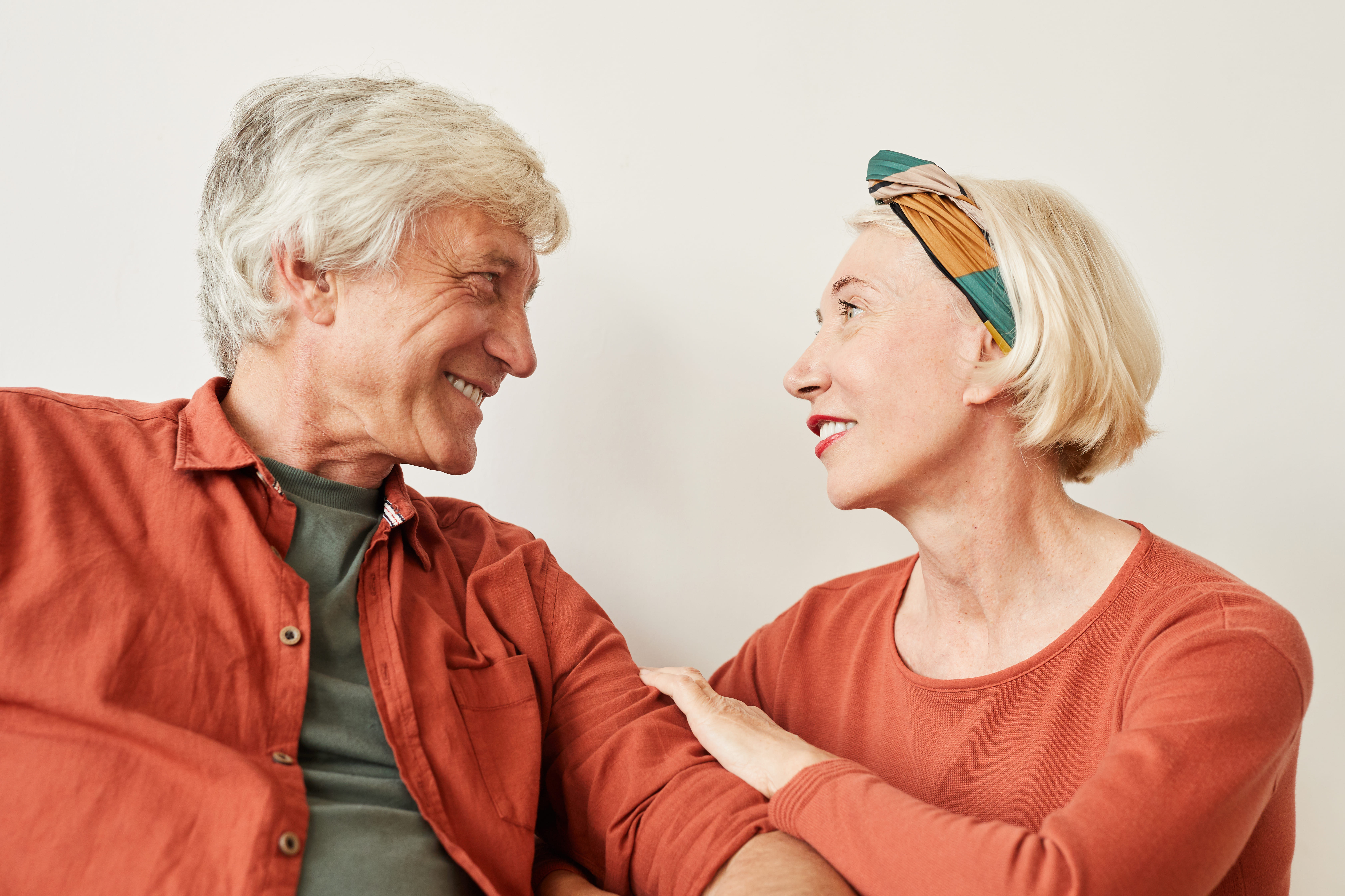 Smiling older couple facing each other, woman resting hand on man's arm, both wearing orange tops.