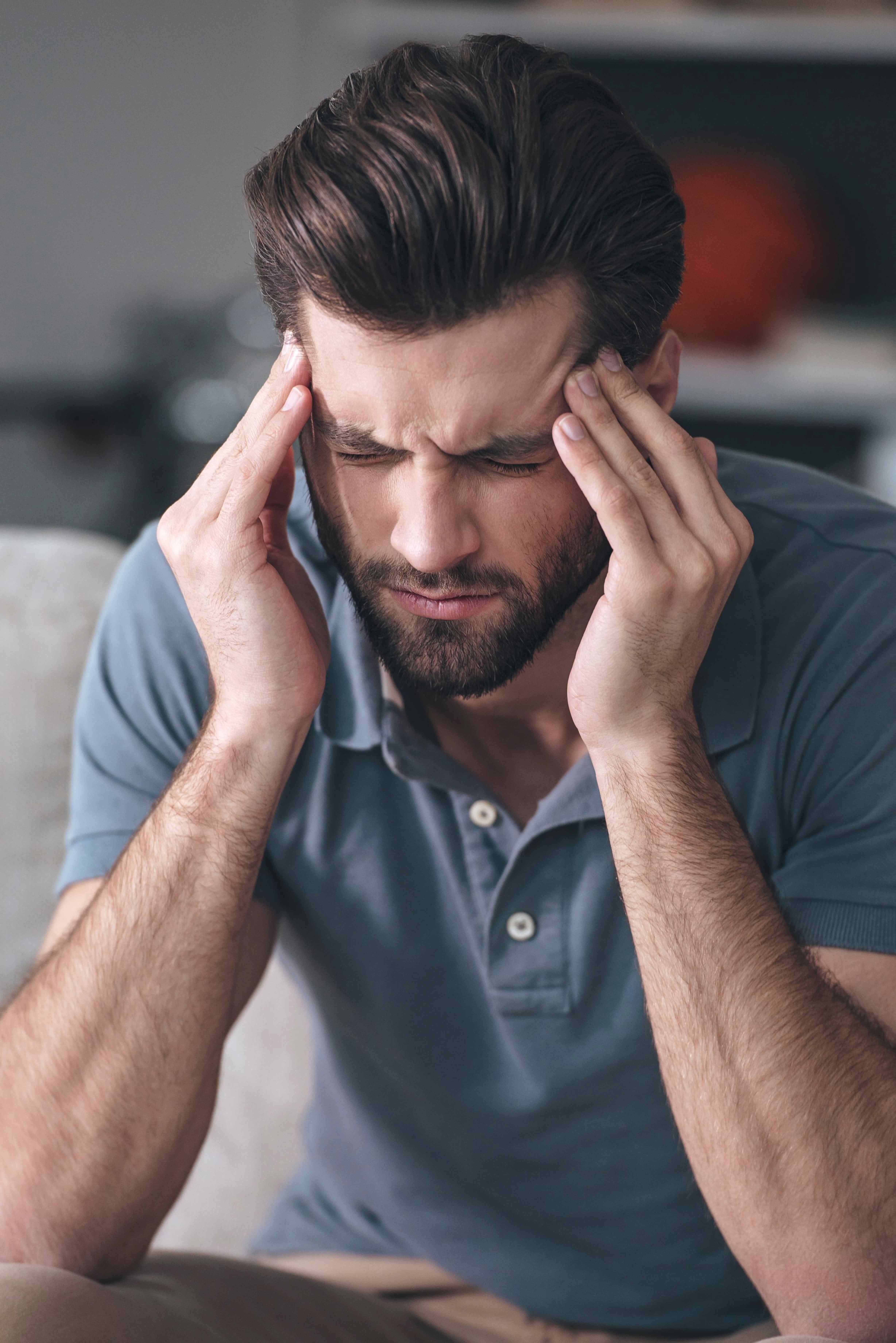 Man with closed eyes pressing his temples, appearing to have a headache or stress indoors.