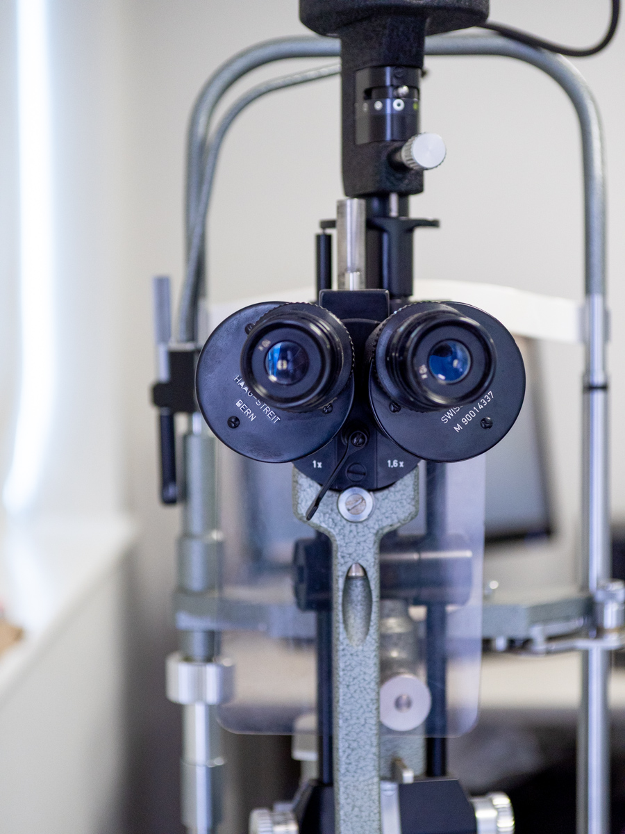 Close-up of a slit lamp microscope used in eye exams with dual eyepieces and adjustment knobs.