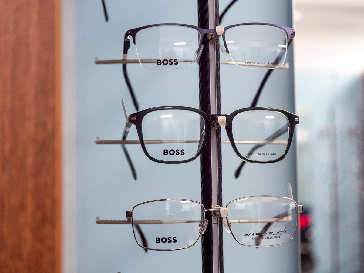 Three pairs of Boss branded eyeglasses displayed vertically on a stand with blue background.