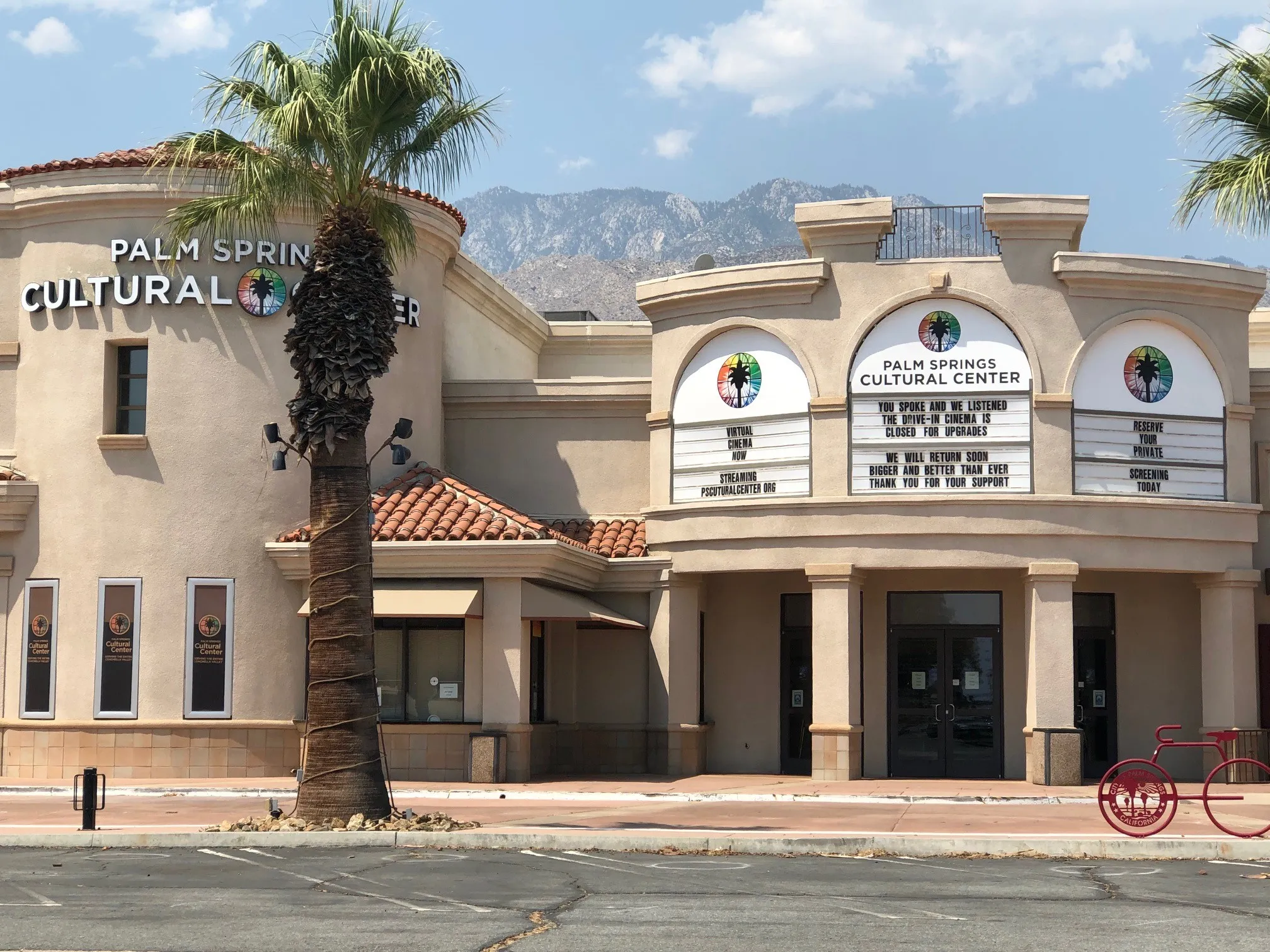 Exterior view of the Palm Springs Cultural Center building with palm trees and mountains in the background.