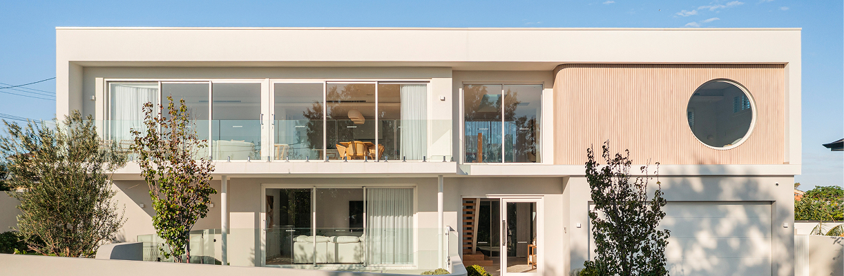 Modern two-story house with large glass windows, balcony with glass railing, and a circular window on the upper right side.