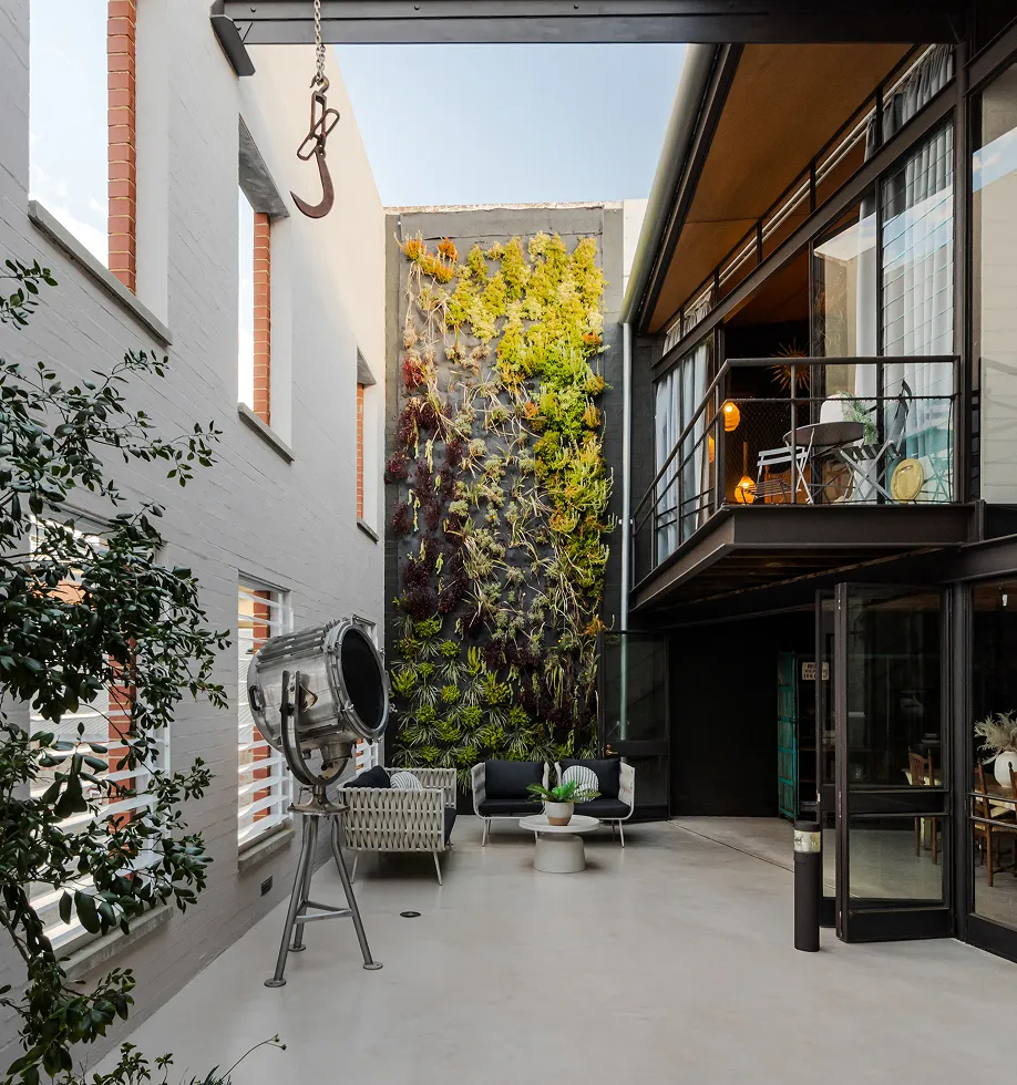 Modern courtyard with vertical garden, outdoor seating, tall windows, and industrial-style balcony on the right.