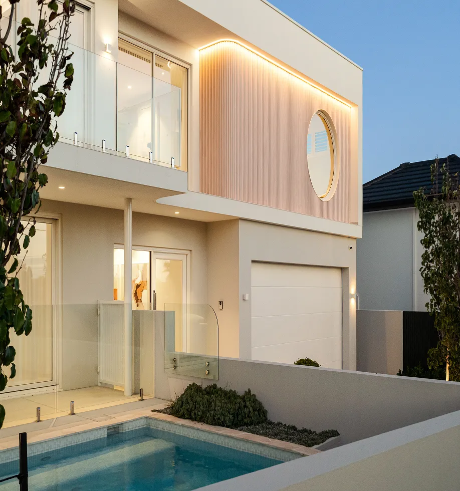 Modern two-story house exterior in the evening with a small pool, glass balcony, and illuminated circular window detail.