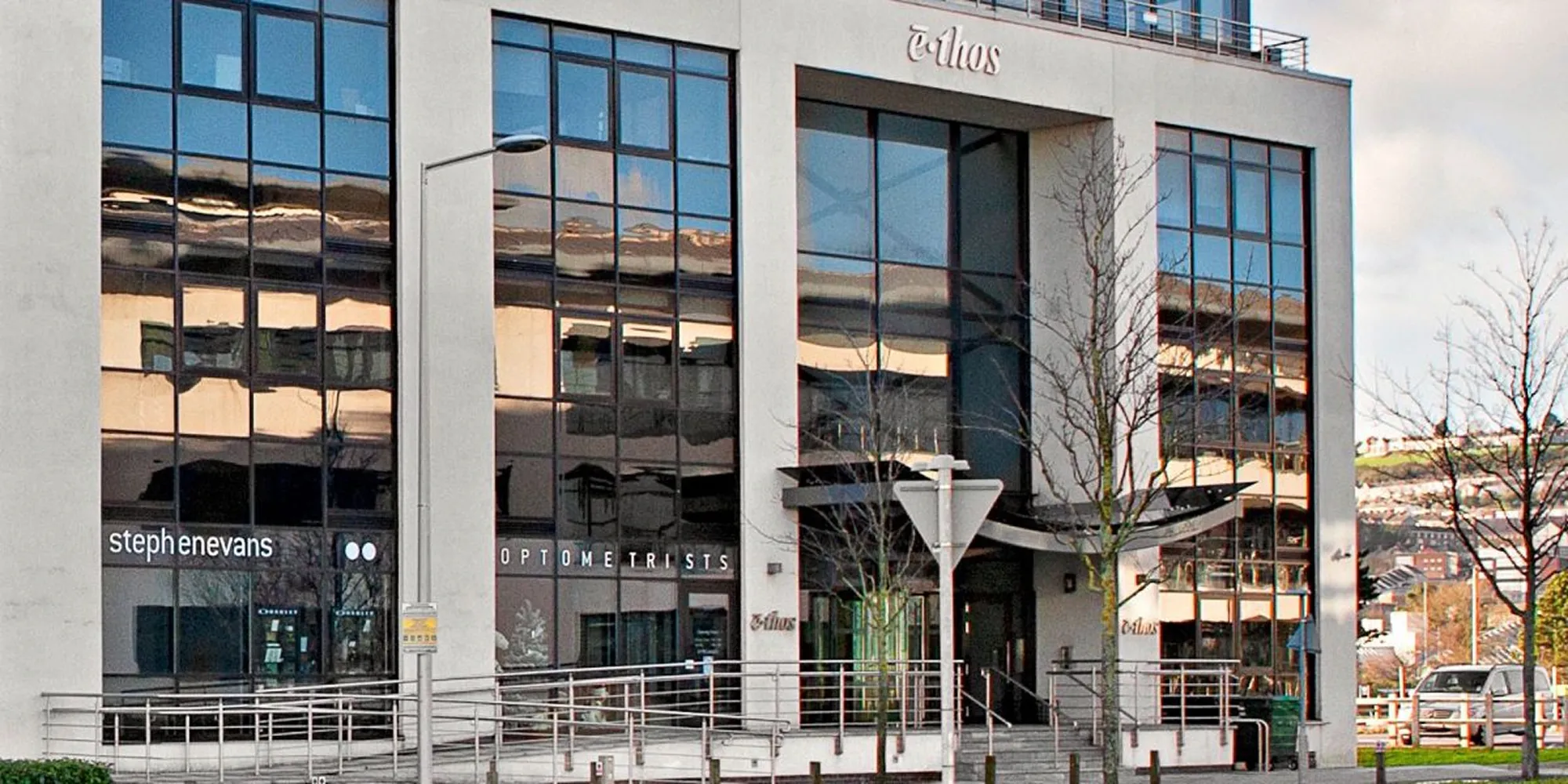 Modern commercial building with large reflective windows and signs for Stephen Evans Optometrists.
