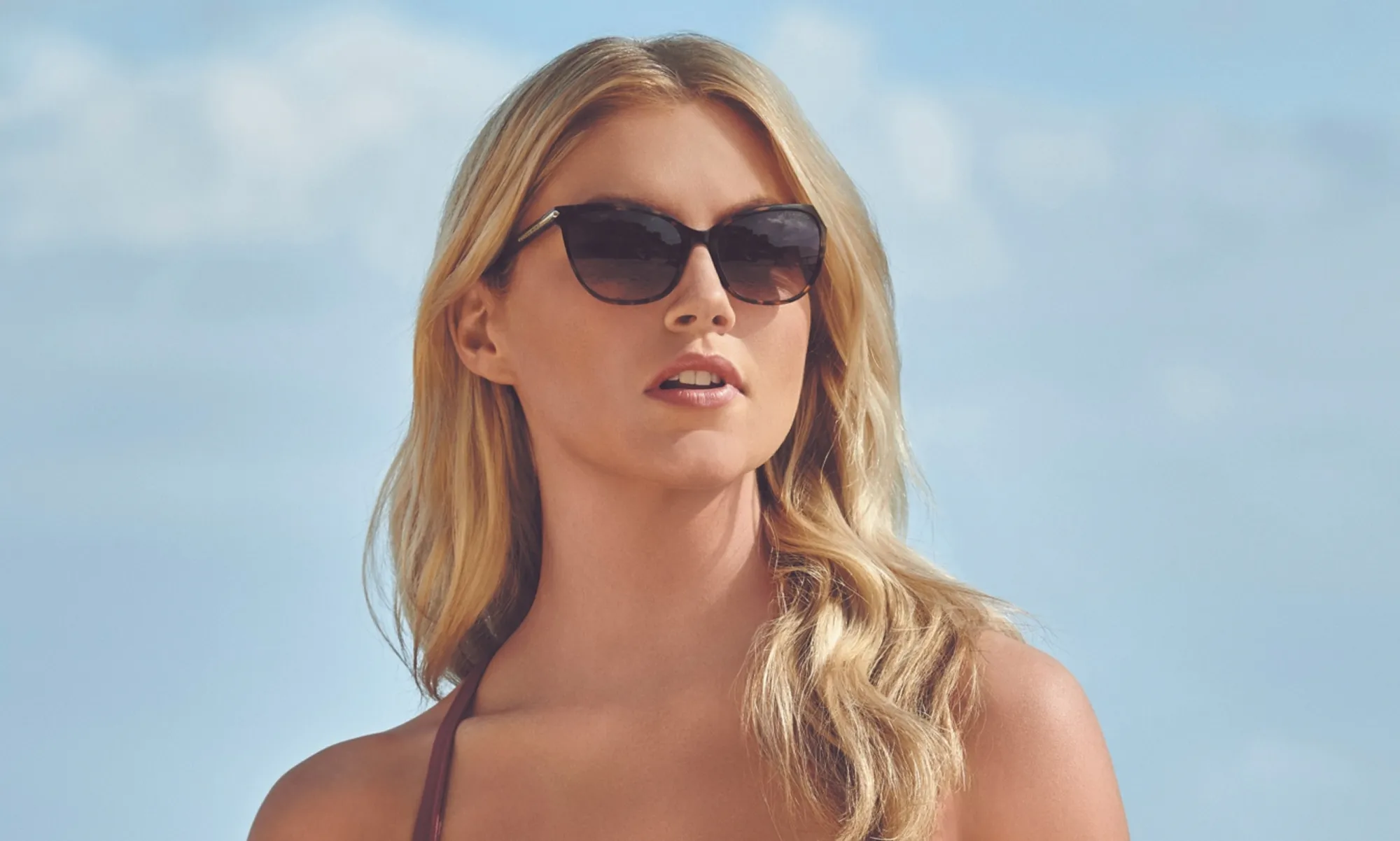 Blonde woman wearing tortoiseshell sunglasses facing forward against a clear blue sky