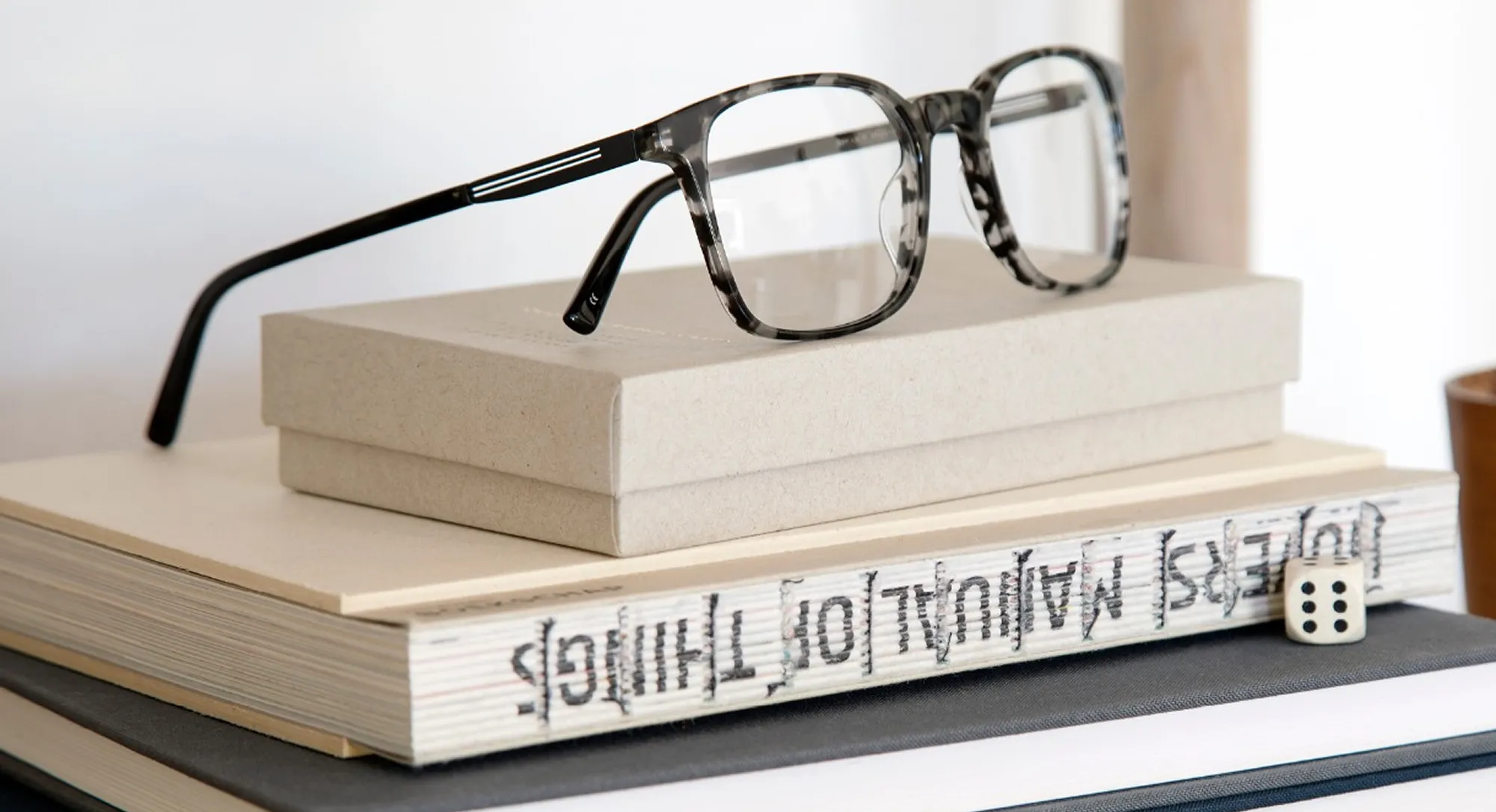 Gray tortoiseshell eyeglasses resting on a stack of books and a box.