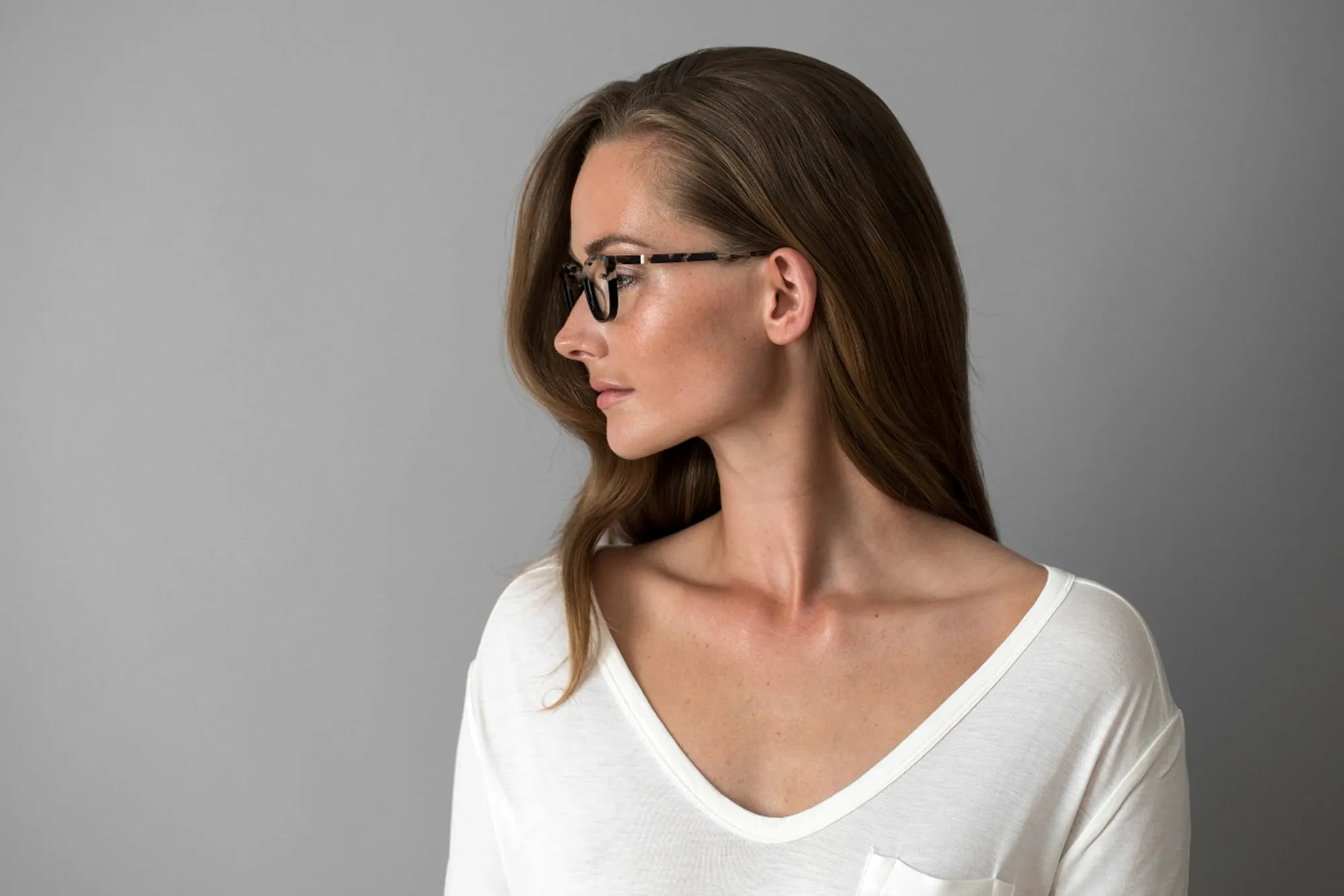 Side profile of a woman wearing black eyeglasses with patterned temples against a gray background.