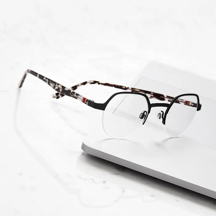 Black half-rim eyeglasses with patterned temples resting on a white surface.