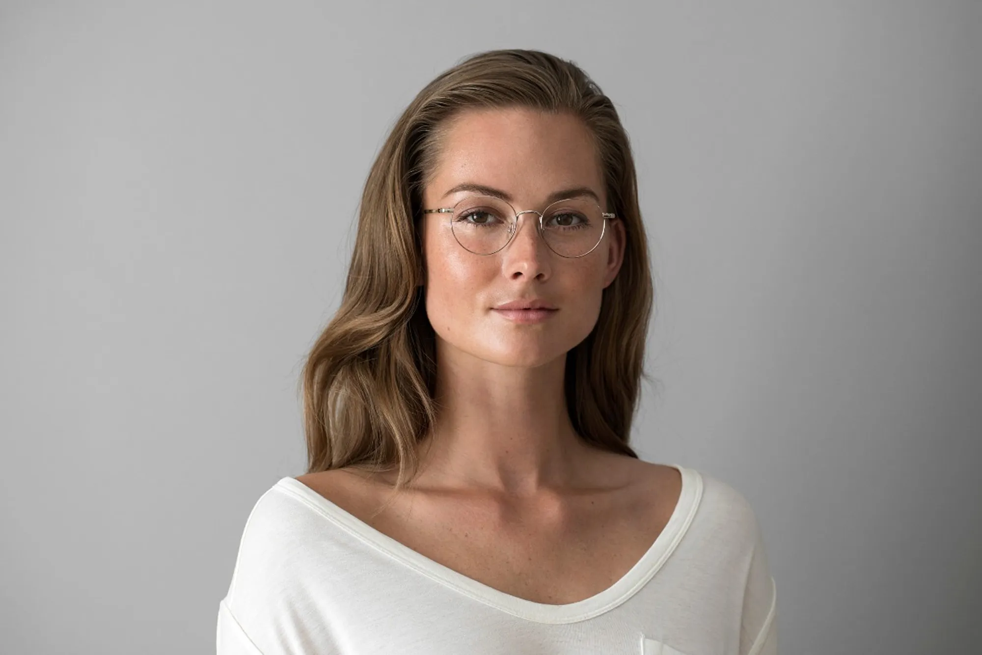Woman wearing thin round metal eyeglasses against a gray background.