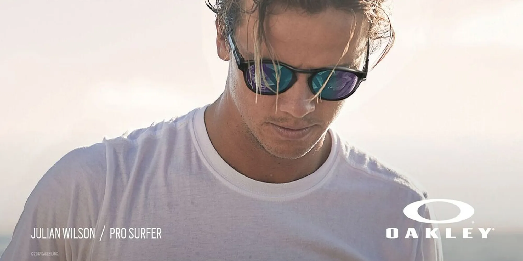 Julian Wilson wearing reflective Oakley sunglasses and a white shirt, looking down.