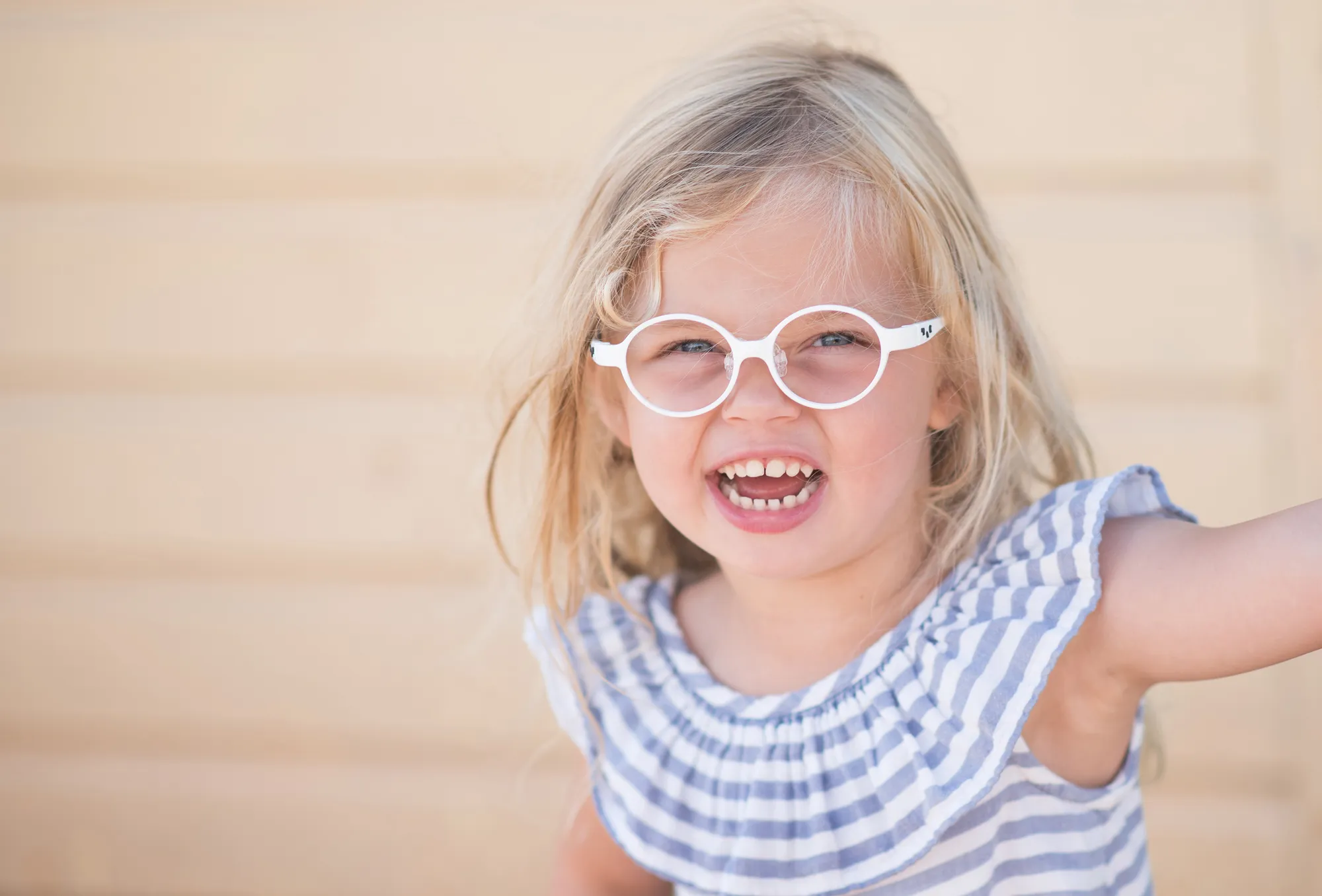 Smiling young child wearing round white eyeglasses and a striped dress.