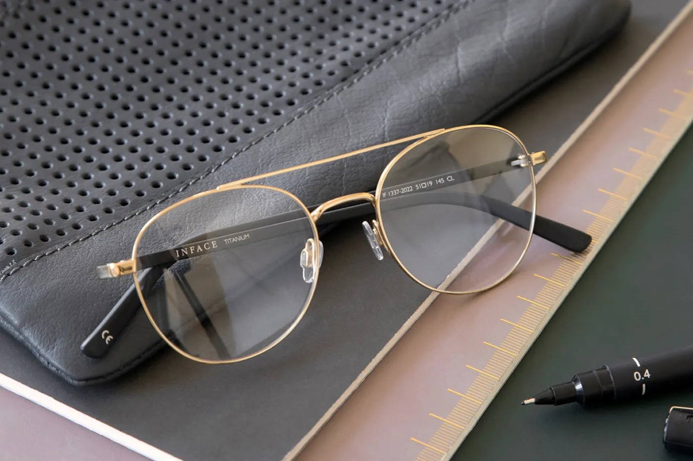 Inface titanium eyeglasses with gold aviator frames resting on a leather notebook