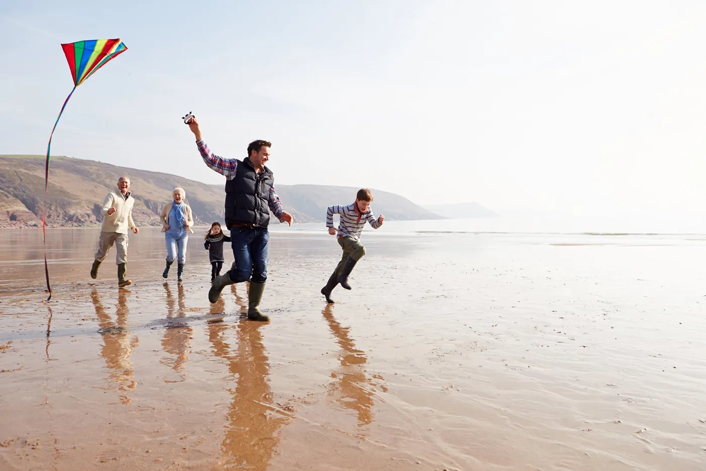 Multi-generational family running along a beach flying a colourful kite