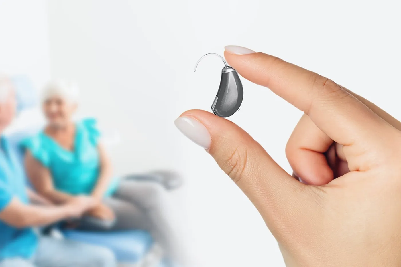 Hand holding a small hearing aid with an older couple blurred in the background