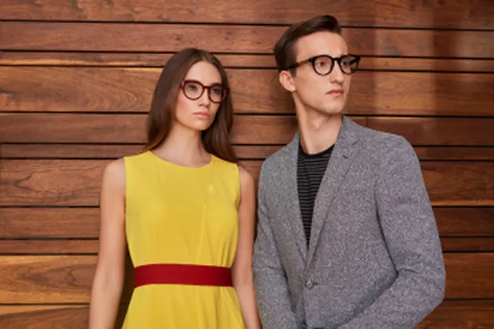 Man and woman in glasses standing before a wooden wall