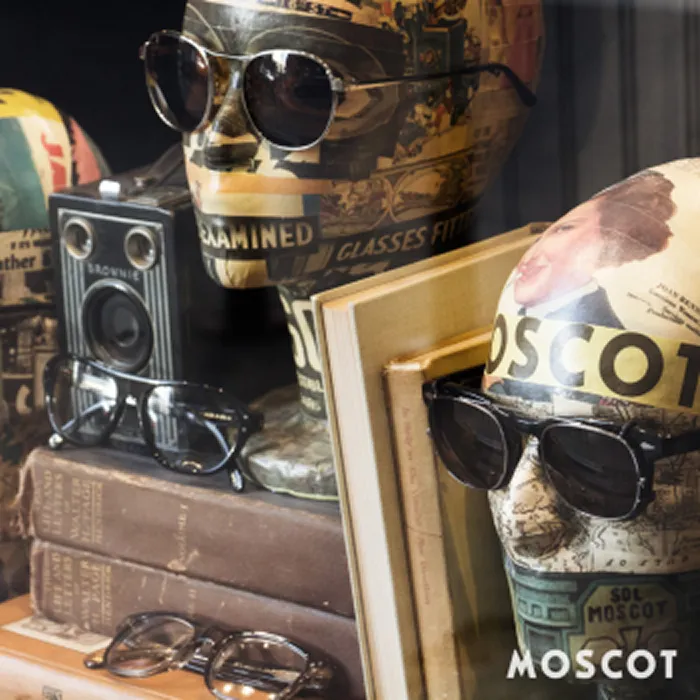Mannequin heads in MOSCOT sunglasses among vintage books and a camera.