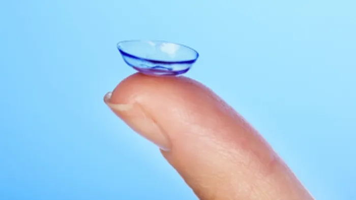 Clear contact lens resting on the tip of a person's finger against a blue background.