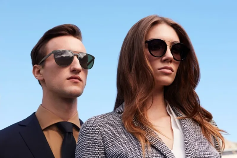Man and woman wearing sunglasses and stylish outfits against a clear blue sky.