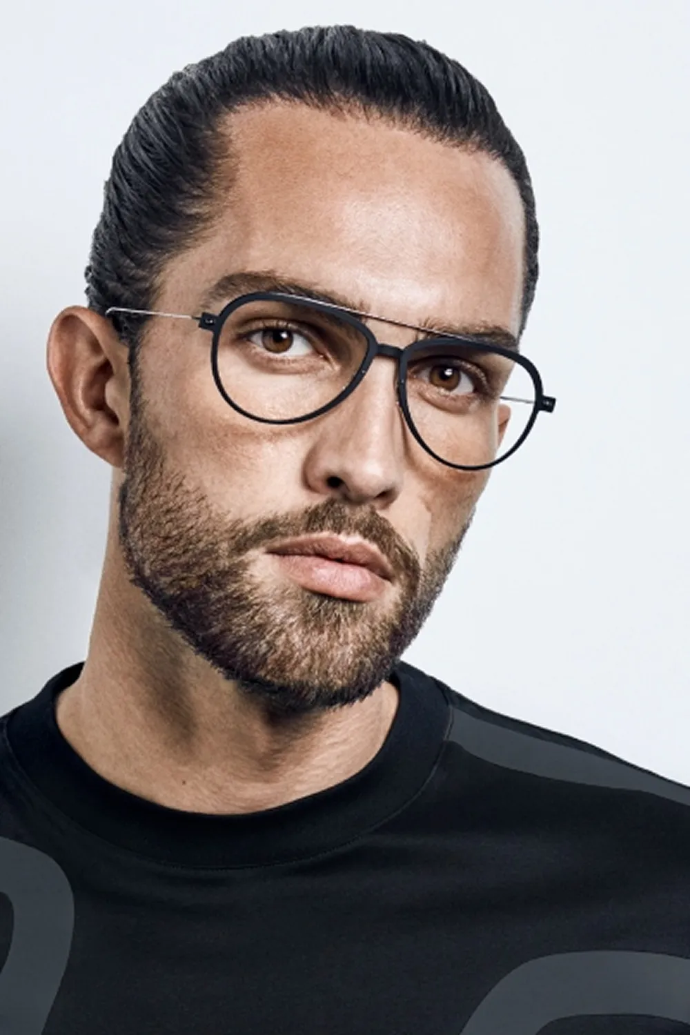 Bearded man with hair tied back wearing round black glasses and a black shirt.