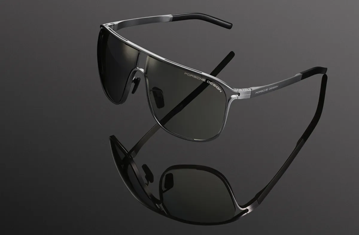 Porsche Design sleek silver-framed sunglasses with dark lenses on a reflective black surface.