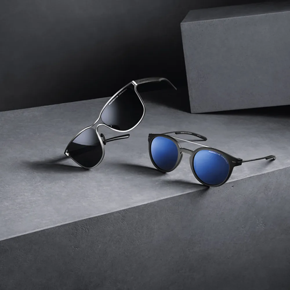 Two pairs of stylish sunglasses, one with black lenses and one with blue lenses, placed on a gray surface.