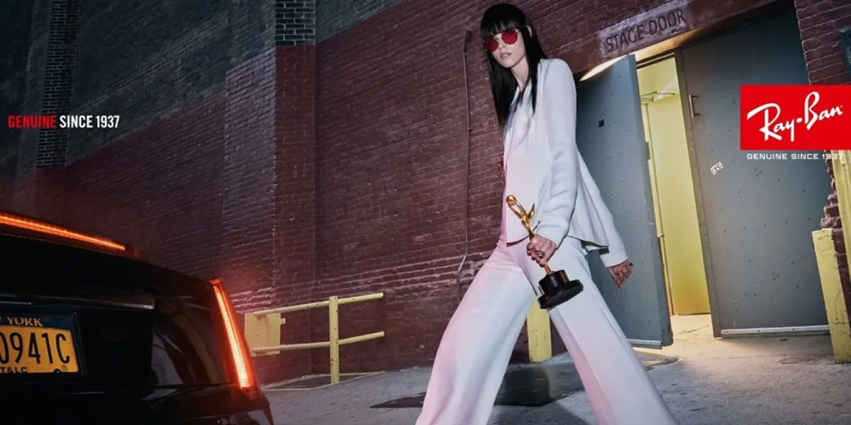 Stylish woman in white suit and red sunglasses holding a trophy walking near a stage door at night.