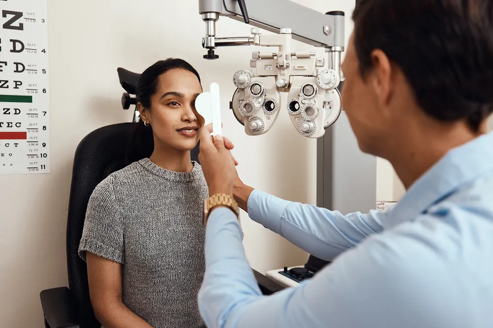 Optometrist performing an eye test on a female patient with a phoropter and eye chart nearby.
