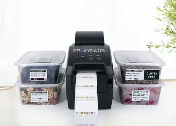 Label printer with printed colorful barcode labels and clear containers of food including granola and blueberries with gluten-free stickers.