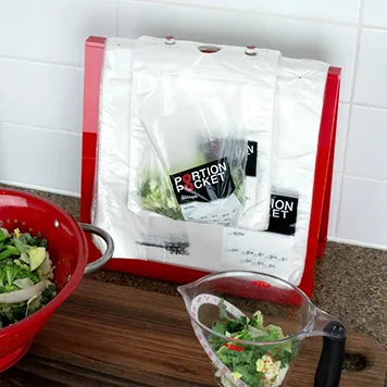 Portion Pocket vacuum-sealed kitchen bags on a countertop next to a red colander and a glass measuring cup with chopped vegetables.