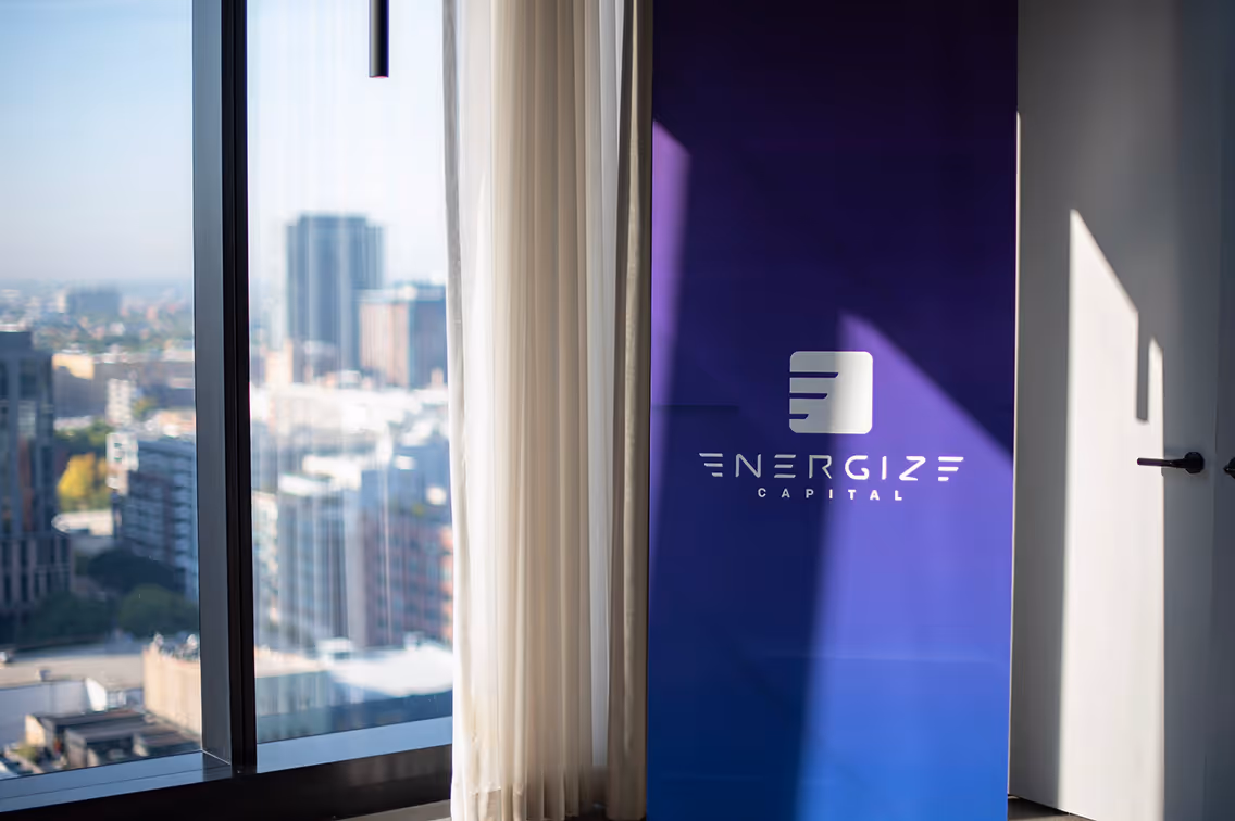 Purple and blue gradient banner with the white Energize Capital logo next to a window overlooking a cityscape.