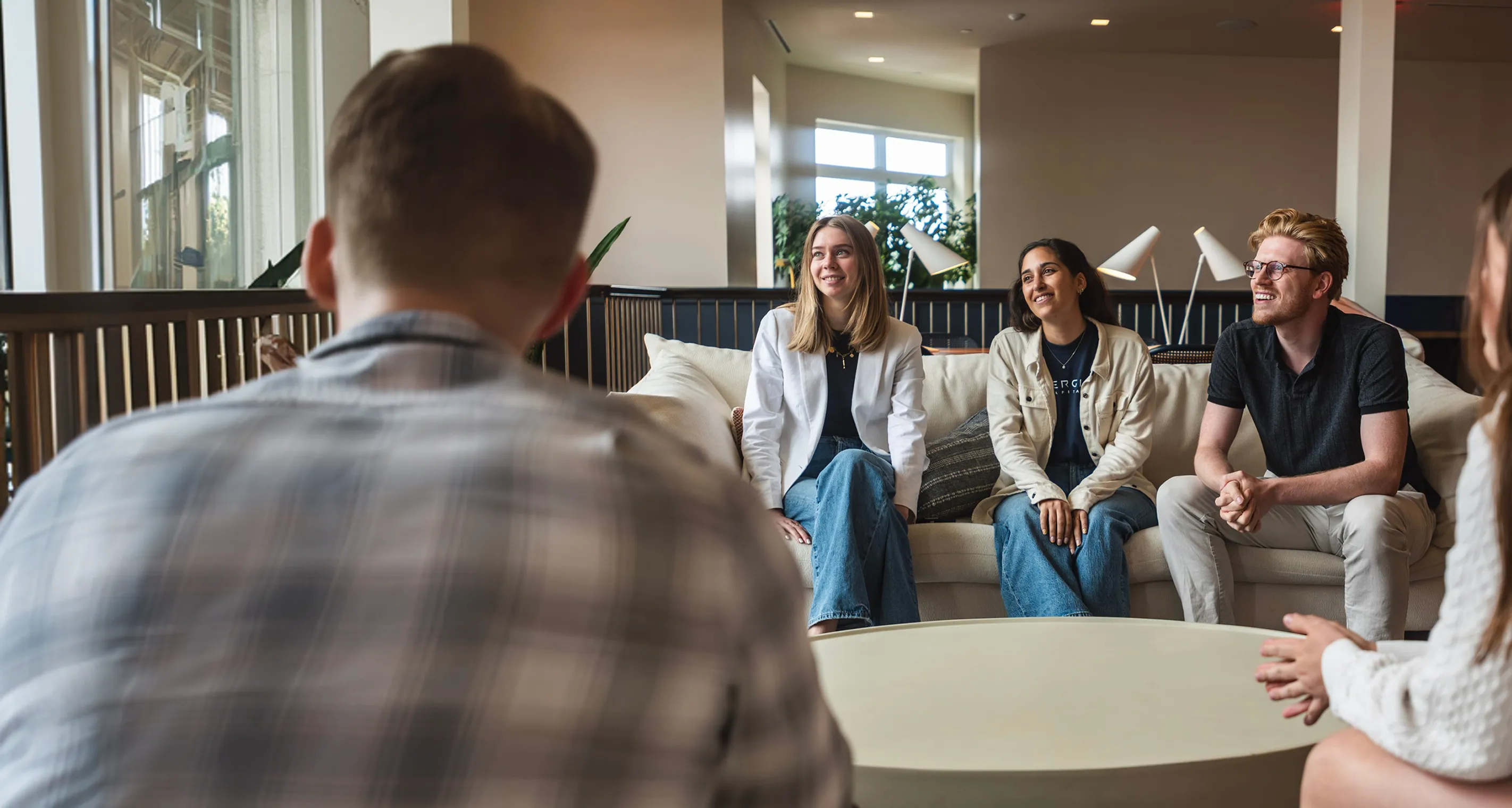 Group of five young adults sitting and talking in a modern, bright living room with natural light.