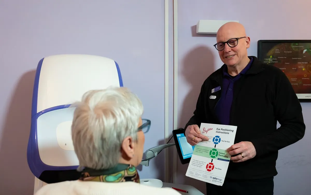 An optometrist explains eye positioning instructions to a patient sitting in front of an eye exam machine.