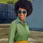 Smiling woman with curly hair wearing blue sunglasses, green shirt, and yellow belt standing outdoors against a blurred background.
