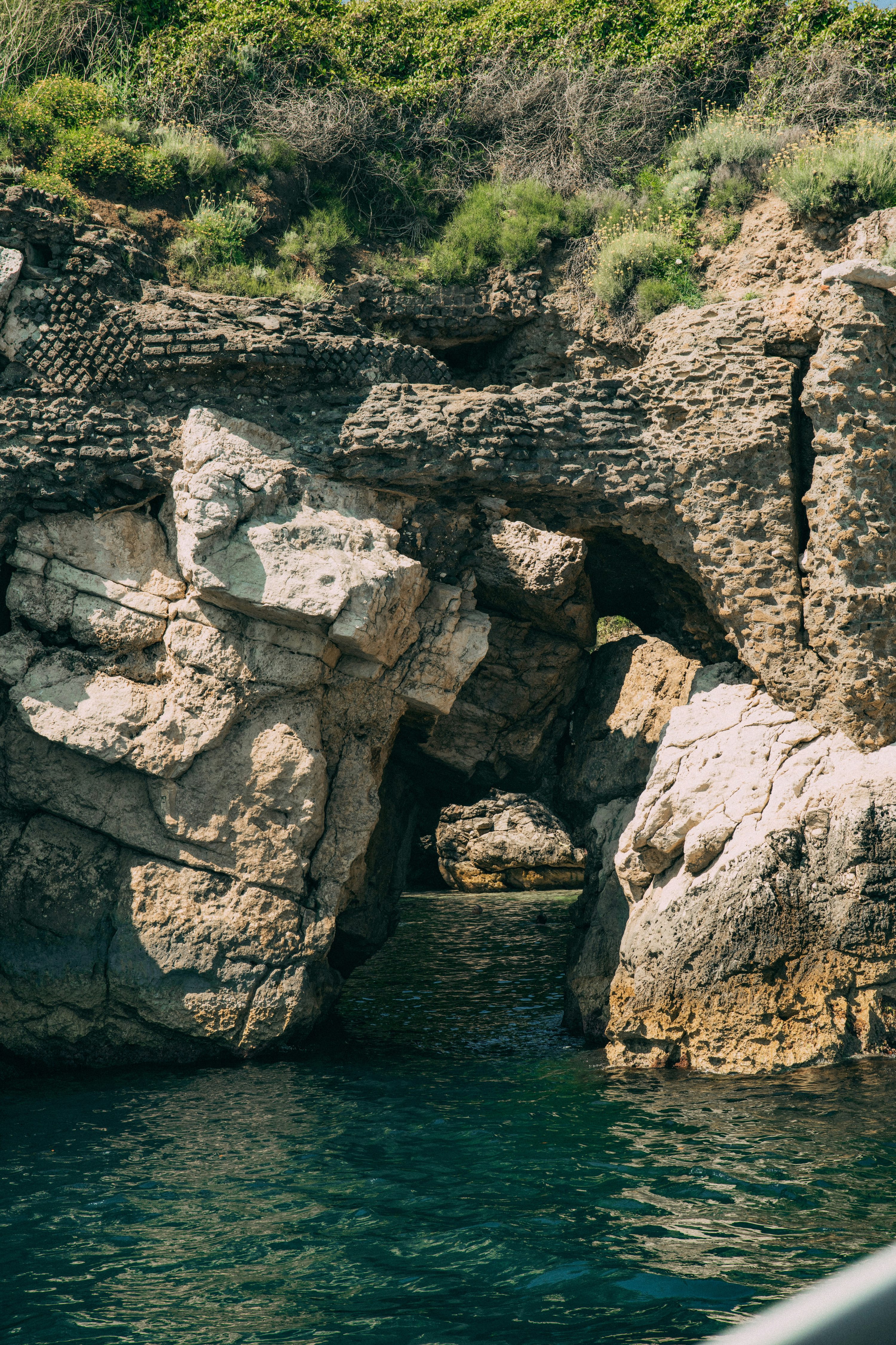 Rocky coastal arch with clear blue-green water and green vegetation above the rocks.